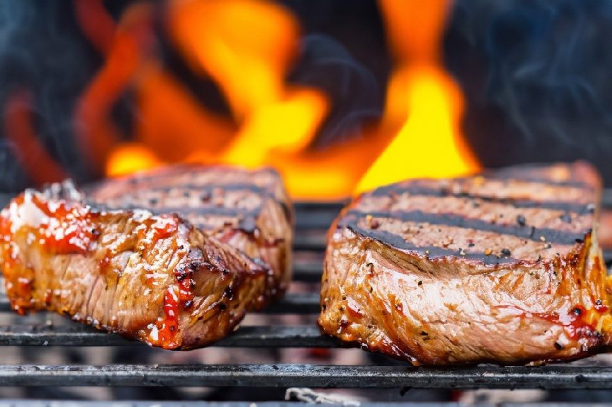 two steaks on grill with flames